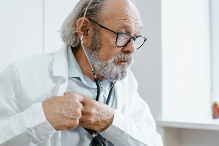 Senior male doctor checking health with stethoscope indoors.
